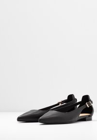 Schwarze Ballerina-F flats aus Leder mit spitzem Zehenbereich, verstellbarem Riemen und kleinem Blockabsatz. Glatte Textur mit minimaler Detailierung.