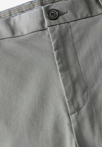 Tissu texturé gris en gros plan d'une paire de pantalons avec un bouton, des coutures visibles et une poche. Design simple et fonctionnel.