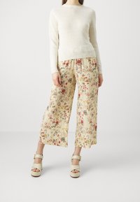 Pull en maille beige clair associé à un pantalon large à imprimé floral crème, orné de fleurs multicolores et à la coupe décontractée. Sandales épaisses crème.