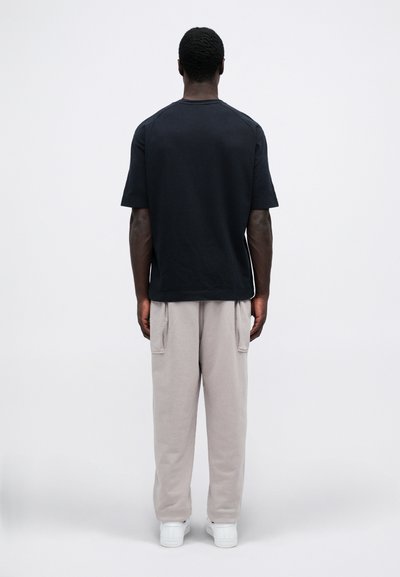 Mørkeblå kortermet t-skjorte og lysegrå joggebukser, kombinert med hvite sneakers, sett fra baksiden mot en ensfarget bakgrunn.