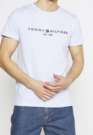 Helles blaues T-Shirt mit kurzen Ärmeln aus Baumwolle, mit einem bedruckten Tommy Hilfiger-Logo in Schwarz und Rot auf der Brust. Klassischer Rundhalsausschnitt.