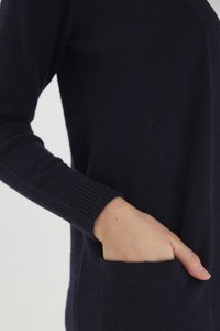 Cárdigan de punto azul marino con puños acanalados, que cuenta con un bolsillo lateral. La textura parece suave y ligeramente difusa.