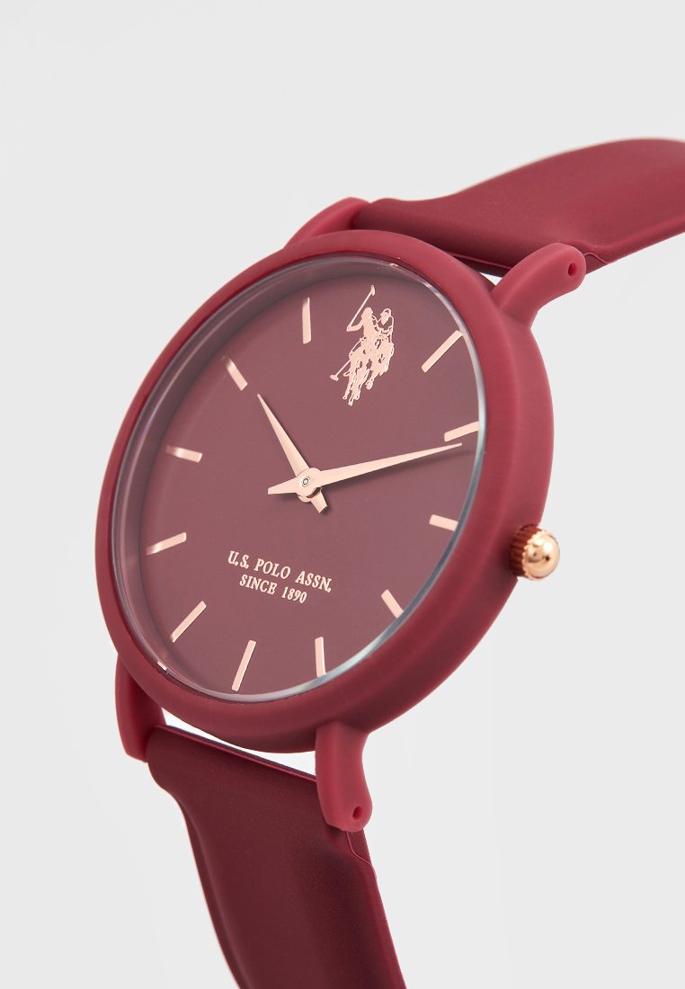 Bordeauxfarbene Silikon-Uhr mit passendem Ziffernblatt, goldfarbigen Akzenten, einfachen Stundenmarkierungen und Logodetail. Glattes, flexibles Armbanddesign.