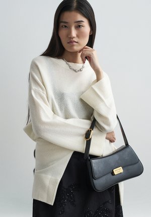 Overdimensioneret off-white sweater med ribbet kant, parret med en sort lædertaske med guldaccent og en struktureret sort nederdel.