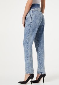 Jeans de lavado claro, de talle alto, con una cintura elástica, piernas rectas y un ligero desgaste. Combinados con zapatos de tacón alto negros.