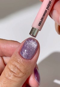 Mini aplikator do makaronów trzymany nad ręką z błyszczącym, lawendowym wzorem na paznokciach. Paznokieć ma gładką teksturę i błyszczące wykończenie.