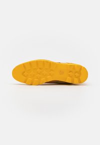 Suela de zapato de goma amarilla con patrón texturizado y prominentes tacos de tracción, que ofrecen un agarre y una estabilidad mejorados. Bordes suaves, diseño duradero.