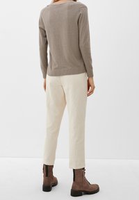 Pull en maille taupe clair, avec un col rond et un ourlet côtelé. Associé à un pantalon en velours côtelé crème et des bottines marron à lacets.