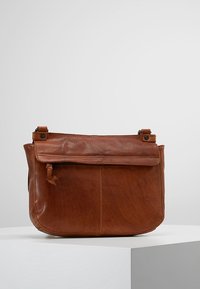 Brun læder crossbody taske med flaplukning, frontlomme og slankt design. Glat tekstur og synlige syninger. Justerbar rem.