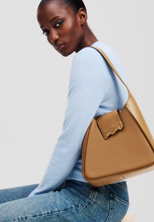 Tan triangular handbag with a smooth leather finish, featuring a flap closure with gold signature hardware. Worn on a shoulder.