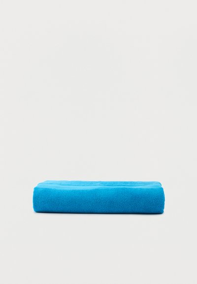 Serviette bleue vif pliée sur un fond gris clair uni, montrant la texture et l'épaisseur.