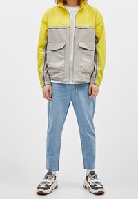 Väriblokkipaita, jossa keltainen yläosa ja harmaa alaosa, etutaskut ja sileä pinta. Yhdistetty vaaleansinisiin farkkuihin ja paksupohjaisiin lenkkareihin.