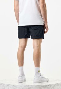 Navy blue swim shorts with a textured surface, plain design, and side pockets; paired with white sneakers and crew socks.