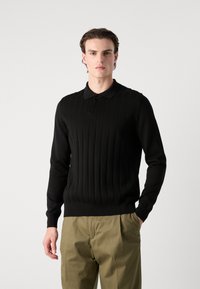 Pulover polo negru cu maneci lungi, textură cu nervuri verticale, material moale și guler clasic, asociat cu pantaloni de culoare verde măsliniu deschis.
