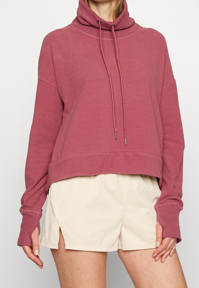 Sweatshirt à capuche rose, avec une coupe décontractée, un design court et des détails à cordonnet. Associé à un short crème.