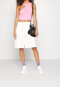Roze geribbelde crop top met uitsnijding, gecombineerd met witte knielange shorts. Draagt witte sneakers en paarse sokken, terwijl ze een zwarte tas meedraagt.