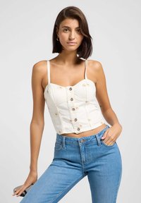 Hvit kort denimtopp med justerbare stropper, frontknapper og blomsterdetaljer; kombinert med blå høyt midje jeans.