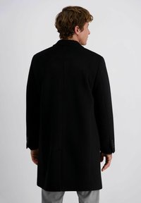 Zwarte wolmix jas met een getailleerd ontwerp, rechte snit en minimalistische details. Lange mouwen met knoopaccenten, halverwege de dijen.