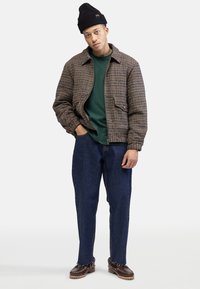 Brown and beige checked jacket, green shirt, blue loose-fit jeans, and brown shoes. Jacket has front pockets, and a collar, and is quilted.