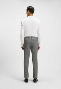 Biała koszula z długim rękawem w połączeniu z szarymi spodniami w kratę, posiadającymi dwie tylne kieszenie, dopasowany krój i czarne buty.