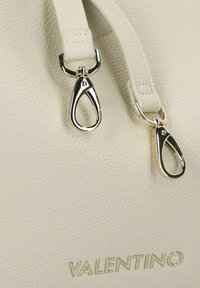 Cremefarben-Handtasche aus Leder mit silberfarbenen Beschlägen und Clip-Details. Die strukturierte Oberfläche wird von einem goldfarbenen "VALENTINO"-Logo akzentuiert.