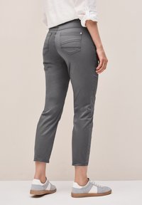 Pantalones de mezclilla gris con un corte ajustado, piernas cónicas, diseño de cinco bolsillos y detalles de costura sutiles, combinados con zapatillas gris claro.