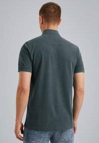 Polo shirt verde scuro a maniche corte, con colletto classico e finitura pulita e testurizzata. Design semplice, senza motivi visibili o accenti.