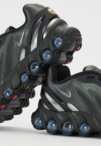 Baskets de sport noires avec un dessus texturé et des accents argentés, un design courbé et des coussinets de amortissement transparent sur la semelle.