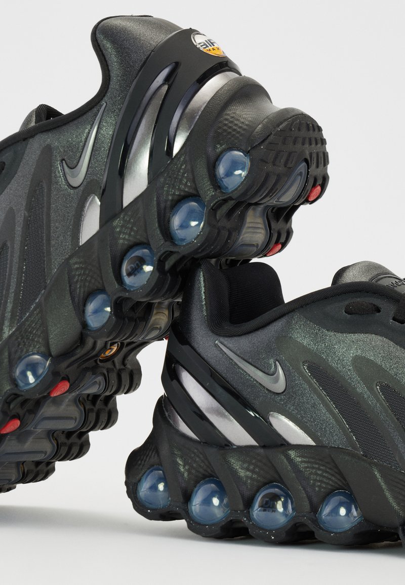 Zapatillas deportivas negras con un upper texturizado y detalles en plateado, un diseño curvado y cápsulas de amortiguación transparentes en la suela.