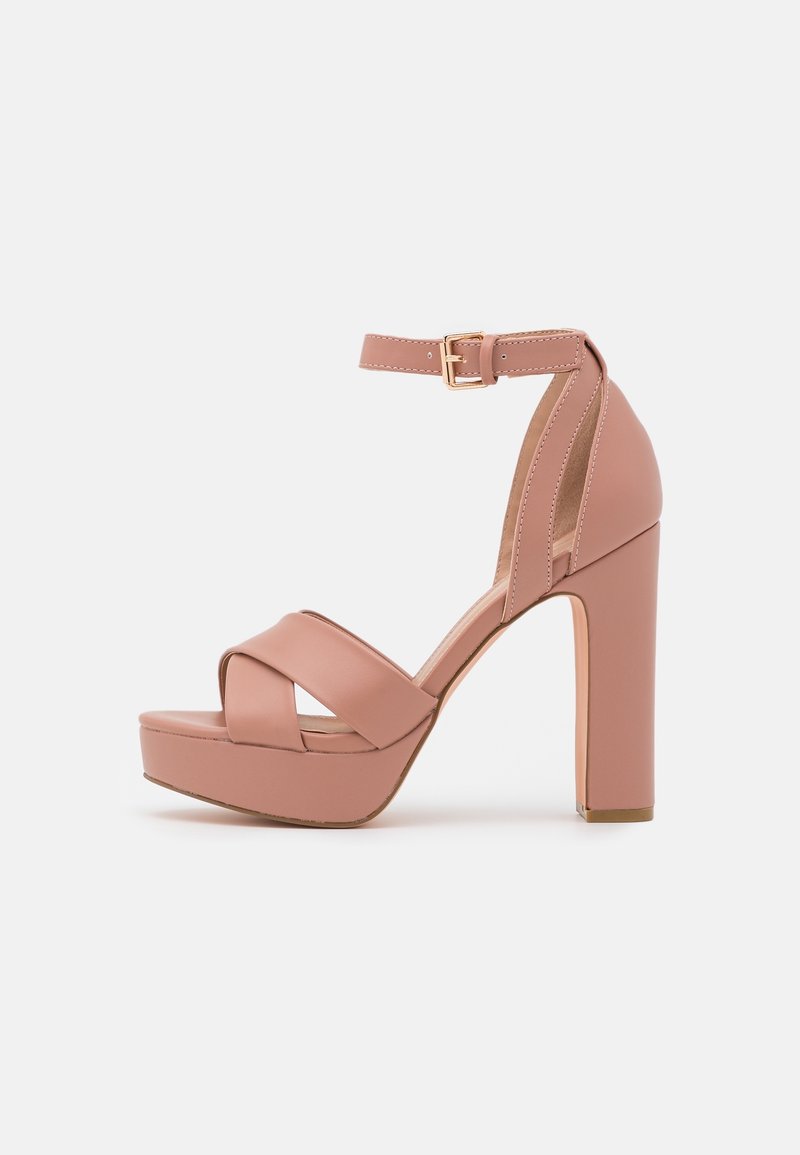 Sandale rose à talon haut avec semelle plateforme, brides croisées à l'avant, bride cheville avec boucle dorée et talon bloc sur fond blanc.