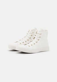 Weiße High-Top-Sneaker aus glattem Material mit gewelltem oberen Rand, goldenen Ösen und strukturiertem Gummisohle.