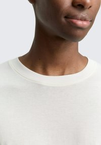 Lichtgewicht, aangesloten katoenen t-shirt met een zachte, gestructureerde oppervlakte en een klassiek ronde halsontwerp in gebroken wit. Minimale stikseldetails.
