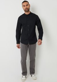 Sort button-up skjorte med lige snit, med en standkrave og en brystlomme, parret med grå bukser og afslappede hvide sneakers.