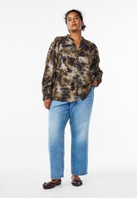 Blusa a maniche lunghe, marrone e beige con motivo, collo e chiusura a bottoni sul fronte, dal taglio morbido, abbinata a jeans dritti blu chiaro.