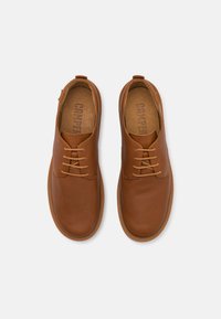 Scarpe di cuoio marrone con una forma arrotondata, design con lacci e una texture liscia. Presentano un sottile logo sulla soletta e uno stile minimalista.