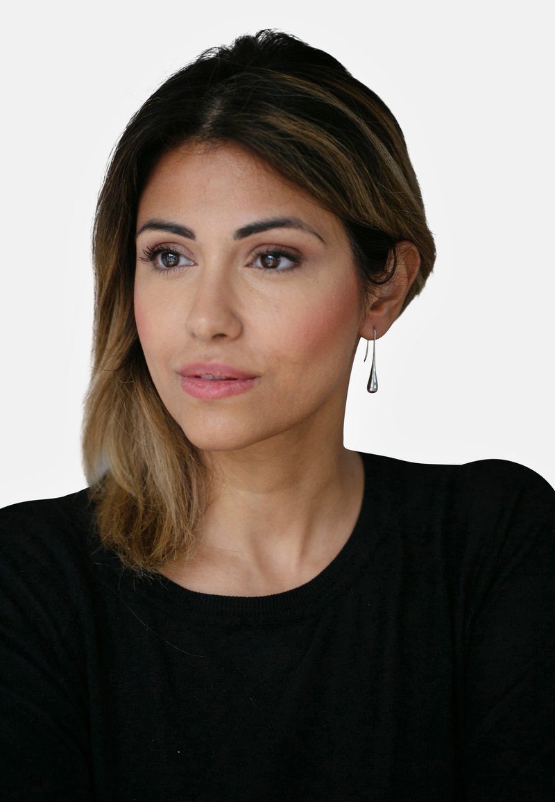 Pendientes en forma de lágrima de plata cuelgan de las orejas. El modelo tiene el cabello largo y oscuro, y lleva un suéter negro con un escote redondo.