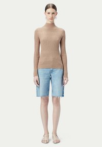 Ljusbrun ribbad långärmad topp i kombination med högmidjade denimshorts. Shorts är lätt fransade i fållen och modellen bär sandaler med remmar.