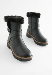 Schwarze Stiefeletten aus Kunstleder mit strukturierter Oberfläche, Kunstfellbesatz, Schnallenakzent und dickem Profilsohle.