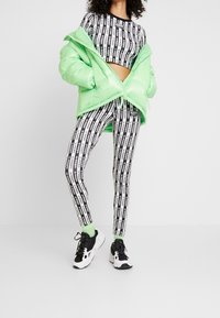 Osoba oblečená v černobílém pruhovaném crop topu s logem Adidas a legínách, se světle zelenou péřovou bundou a odpovídajícími ponožkami, černobílých teniskách.