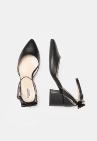 Scarpe nere in pelle con tacco alto, punta affusolata, cinturino alla caviglia e applicazione a fiocco. Presentano un tacco quadrato e robusto con soletta beige.
