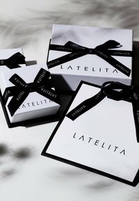 Three gift boxes in white with black accents and ribbons, featuring the brand name "LATELITA" in a modern font. Various sizes and textures.