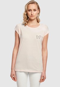 Lyserød bomulds t-shirt med oprullede ærmer og et lille sort sommerfugl-design på venstre bryst. Blød tekstur og afslappet pasform.