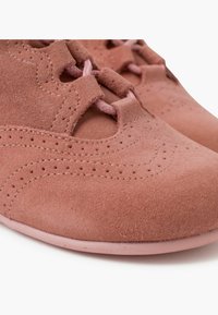 Zapatos de ante rosa con detalles perforados, cordones de tela y punta redondeada. La suave suela rosa complementa la textura blanda.