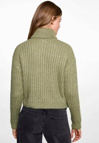 Olivgrön ribbad stickad tröja med hög krage, kort design och sänkt axel, med en strukturerad blond. Justerad passform vid fållen.