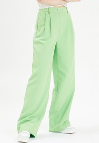 Lichtgroene wijde broek met plooi, gladde textuur en een enkele knoopsluiting bij de tailleband. Gedetailleerd met zijnaad.