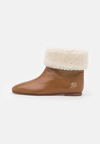 Bottes de cheville en cuir marron avec une manche en fausse fourrure crème, design à bout pointu, semelle plate et broderie de logo discrète sur le côté.