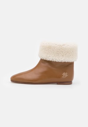 Botas de tobillo de cuero marrón con un puño de piel sintética crema, diseño de punta afilada, suela plana y un sutil bordado de logo en el lateral.