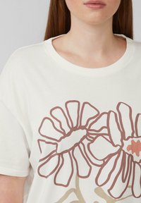 Witte katoenen t-shirt met een bloemenontwerp in bruine en beige tinten. Het heeft een ronde halslijn en korte mouwen.