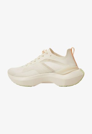 Baskets de sport beige clair avec semelle épaisse, tige en mesh, fermeture à lacets à l'avant, et languette orange au talon, vues de profil.