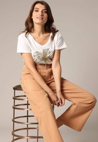 Witte V-hals t-shirt met gouden zebra print; lichtbruine wijde broek; zittend op een metalen kruk; gladde texturen en casual ontwerp.